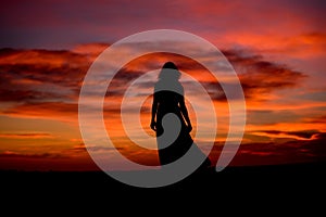 Silhouette of a woman in sunset with dress and hair blow by the wind