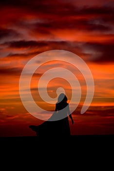 Silhouette of a woman in sunset with dress and hair blow by the wind