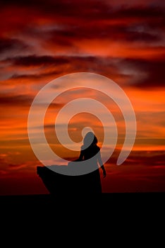 Silhouette of a woman in sunset with dress and hair blow by the wind