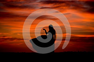 Silhouette of a woman in sunset with dress and hair blow by the wind