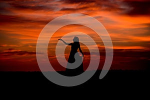 Silhouette of a woman in sunset with dress and hair blow by the wind