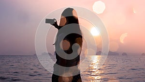 Silhouette woman taking photo of sunrise or sunset sea with bokeh