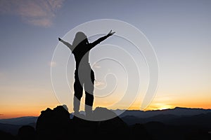 Silhouette of woman on top of the mountain looking to the sun, freedom, pray on top of mountain
