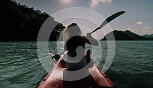 Silhouette of woman tourist raising hands while sailing in canoe along sea bay water to distant hilly island backside