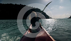 Silhouette of woman tourist raising hands while sailing in canoe along sea bay water to distant hilly island backside