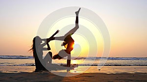 Silhouette of a woman trains a girl to perform acrobatic element on the beach