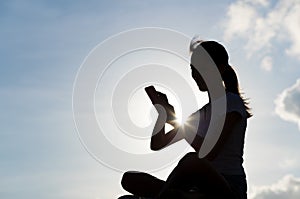 Silhouette of woman using cellphone under skyline in the evening