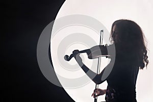 Silhouette of a woman violinist in a white semicircle with smoke on a black background. A concept for music during the