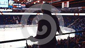 Silhouette of woman walking towards handrailing in sport venue before start of hockey game. Girl watching players having