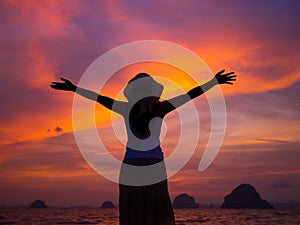 Silhouette of woman wearing hat with open arms under the sunrise near the sea