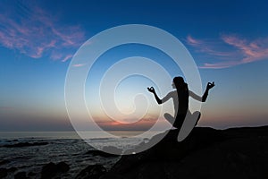 Silhouette of woman yoga in Lotus position on the shore of ocean at evening