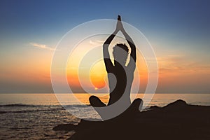 Silhouette of woman yoga in Lotus position on the shore of ocean.