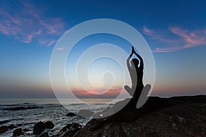 Silhouette of woman yoga position on the shore of ocean at meditation evening