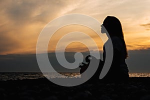 Silhouette of a women in meditation pose on the sea beach during surreal sunset on sea background and dramatic sky. Concept of