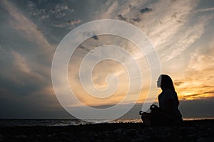 Silhouette of a women in meditation pose on the sea beach during surreal sunset on sea background and dramatic sky. Concept of