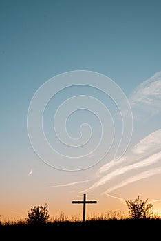 Silhouette of a wooden cross on a grassy hill with a beautiful sky in the background