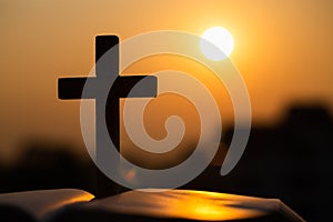 Silhouette of the wooden cross over opened bible with a bright sunrise as background , Christian, god
