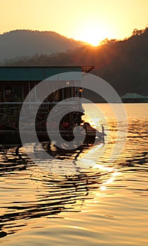 Silhouette of wooden floating house during golden sunset in Mae Ngad Dam and Reservoir