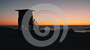 Silhouette of wooden lifeguard house on sandy beach at sunset. Beach safeguard house or shack against beautiful sunset. Wooden hut