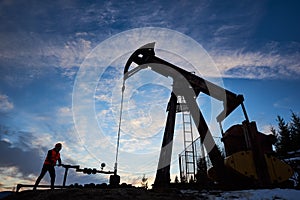 Silhouette of a worker and an oil pump jack on the sunset agains beautiful sky