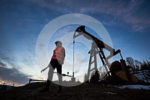 Silhouette of a worker and an oil pump jack on the sunset agains beautiful sky