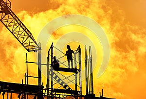 Silhouette workers in construction site with crane on sunset