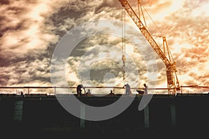 Silhouette of workers on the top of the building construction site with crane and sunset sunlight, image contains film graine.