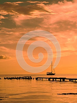 Silhouette of a yacht sailing in a sea and an old wooden pier during the sunset