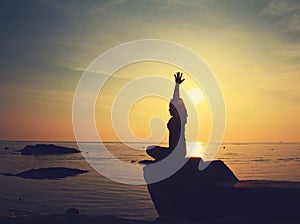 Silhouette yoga girl by the beach at sunrise doing meditation