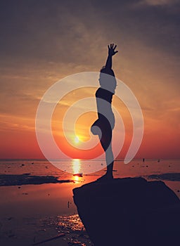 Silhouette yoga girl by the beach at sunrise doing standing tree