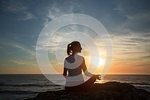 Silhouette of yoga woman meditation on the ocean beach at sunset