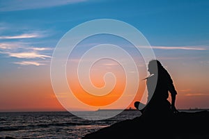 Silhouette of yoga woman meditation on the ocean during sunset.