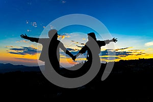 Silhouette of Young Asian Couple Holding Hand at Sunset on Mountain with Blue Sky. Enjoying Peaceful Moment Concept. Relaxing or