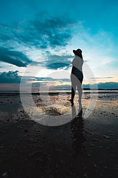 Silhouette of young asian woman standing on the beach and looking at beautiful sea and sky