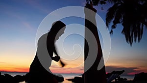 Silhouette of young athletic man is boxing, practices with punching bag on the beach during sunset. Slow motion