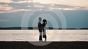 Silhouette Of young attractive couple hugging on the beach on sunset. Man and woman talking on the shore of the river.