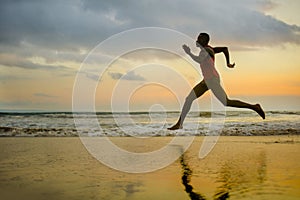 Silhouette of young attractive fit athletic and strong black African American man running at sunset beach training hard and