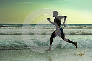 Silhouette of young attractive fit athletic and strong black African American man running at sunset beach training hard and