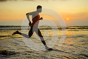 Silhouette of young attractive fit athletic and strong black African American man running at sunset beach training hard and