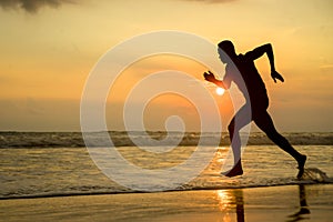 Silhouette of young attractive fit athletic and strong black African American man running at sunset beach training hard and