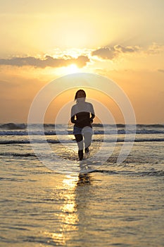 Silhouette of young beautiful and asian woman running free and happy having fun at sunset beach in Bali
