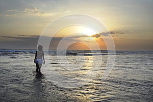 Silhouette of young beautiful asian woman standing on water free and relaxed looking at sun horizon on sunset beach