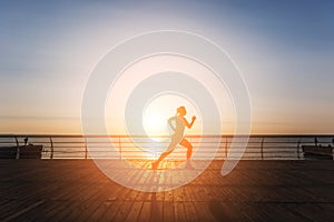 Silhouette of a young beautiful athletic girl with long blond hair in black clothes running at sunrise over the sea