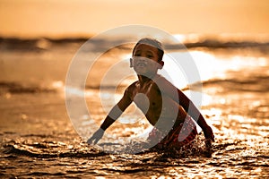 Silhouette of young boy playing crazy happy and free at the beach splashing with water playing with sea waves jumping and having