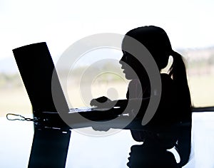 A silhouette of a young child looking on the computer. May depi