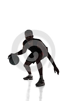 Silhouette of young concentrated young man, basketball player in motion during game, dribbling ball isolated on white