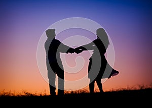 A silhouette of a young couple dancing at sunse