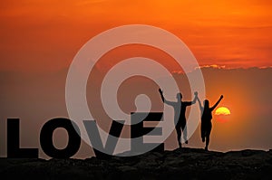 Silhouette young couple in love enjoy good time together during sunset and love text on top Mountain, sky and sunset background.