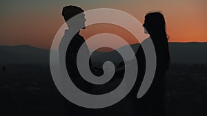 Silhouette of young couple in love enjoying a sunset over the mountains. Vacation, travel, romance, marriage proposal