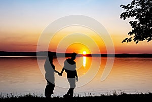 Silhouette of young couple, man and girl, who are watching sunset on shore. Sun setting over horizon